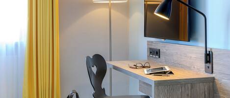 Habitación de hotel con escritorio, silla, lámpara y televisor montado en la pared.