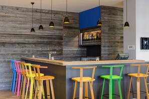 Een bar met houten barkrukken, een toog en hangende pendelverlichting.