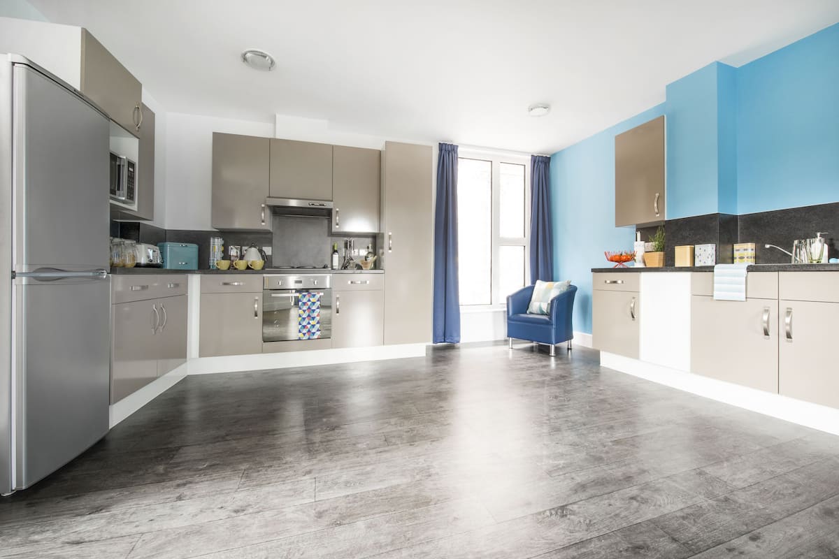 A modern kitchen with stainless steel appliances, a blue chair, and a large window with curtains.