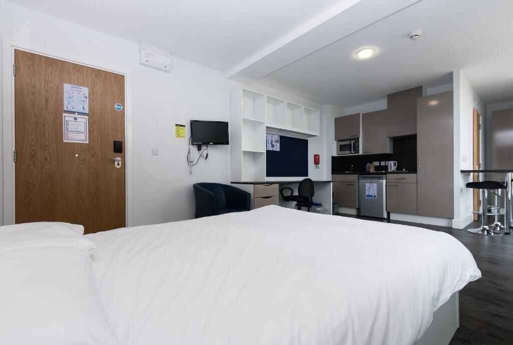 A hotel room with a bed, a desk, a chair, a TV, a microwave, and a small kitchenette.