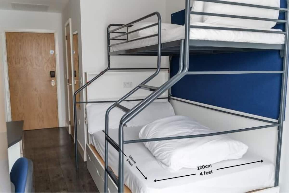 A bunk bed with a desk and chair, a wooden door, and a blue wall.