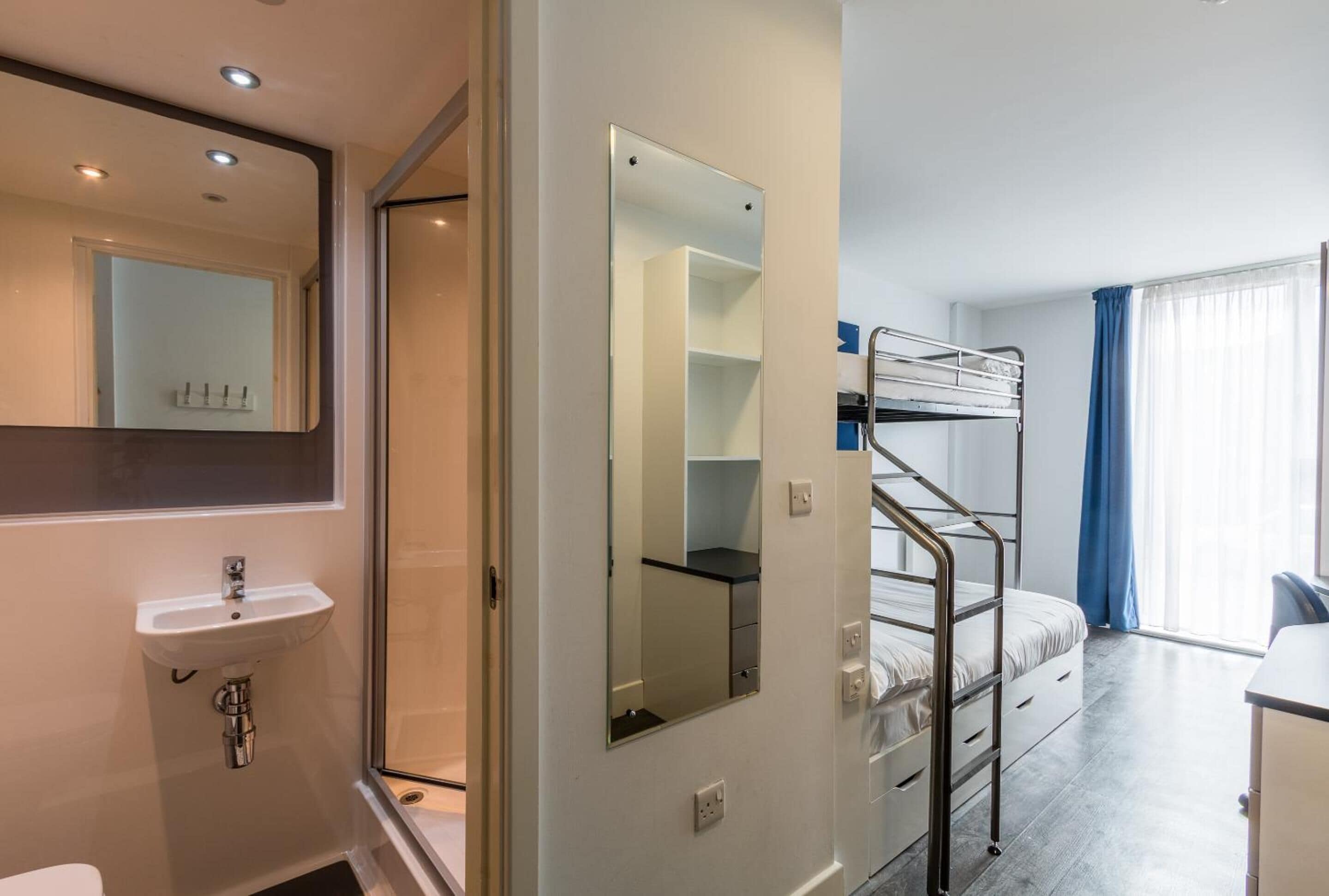 Habitación de hotel con literas, una mesita de noche, un espejo y una ventana con cortinas.