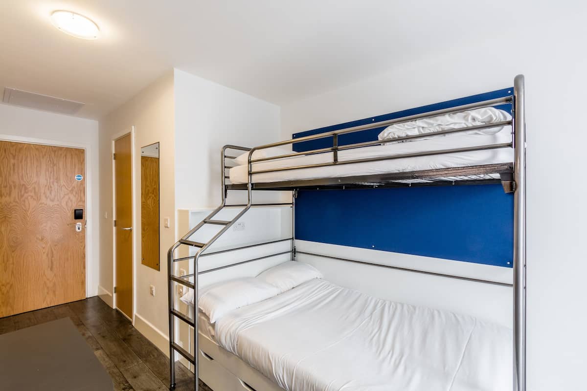 A bunk bed room with a wooden door, a white wall, and a blue headboard.
