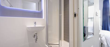 Un baño moderno con cabina de ducha de vidrio, un lavabo blanco y un espejo.