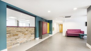 A hallway with a stone wall, a reception desk, a colorful wall display, and a pink couch. - Destiny Student Holyrood - Campus Accommodation (Edinburgh)