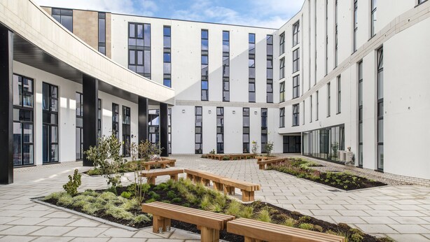 A modern building with a courtyard featuring wooden benches and landscaped gardens. - Destiny Student Holyrood - Campus Accommodation (Edinburgh)