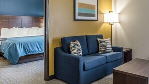 A hotel room with a bed, a blue sofa, a lamp, and a painting on the wall. - MainStay Suites Midland (Midland)