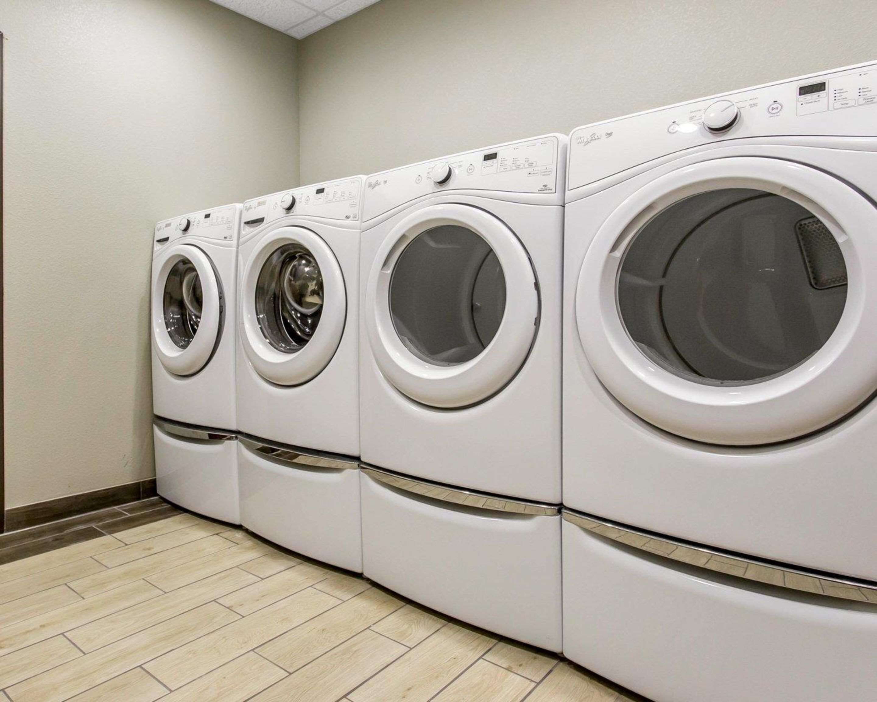 A row of four front-loading washing machines in a laundry room with a tiled floor.