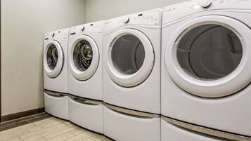 A row of four front-loading washing machines in a laundry room with a tiled floor.