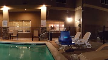 Relax by the pool surrounded by a low wall and lounge chairs under a pergola.