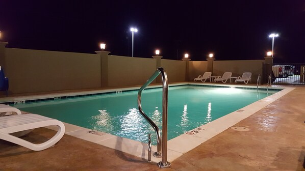 An outdoor swimming pool with a metal ladder, lounge chairs, and a tiled deck.