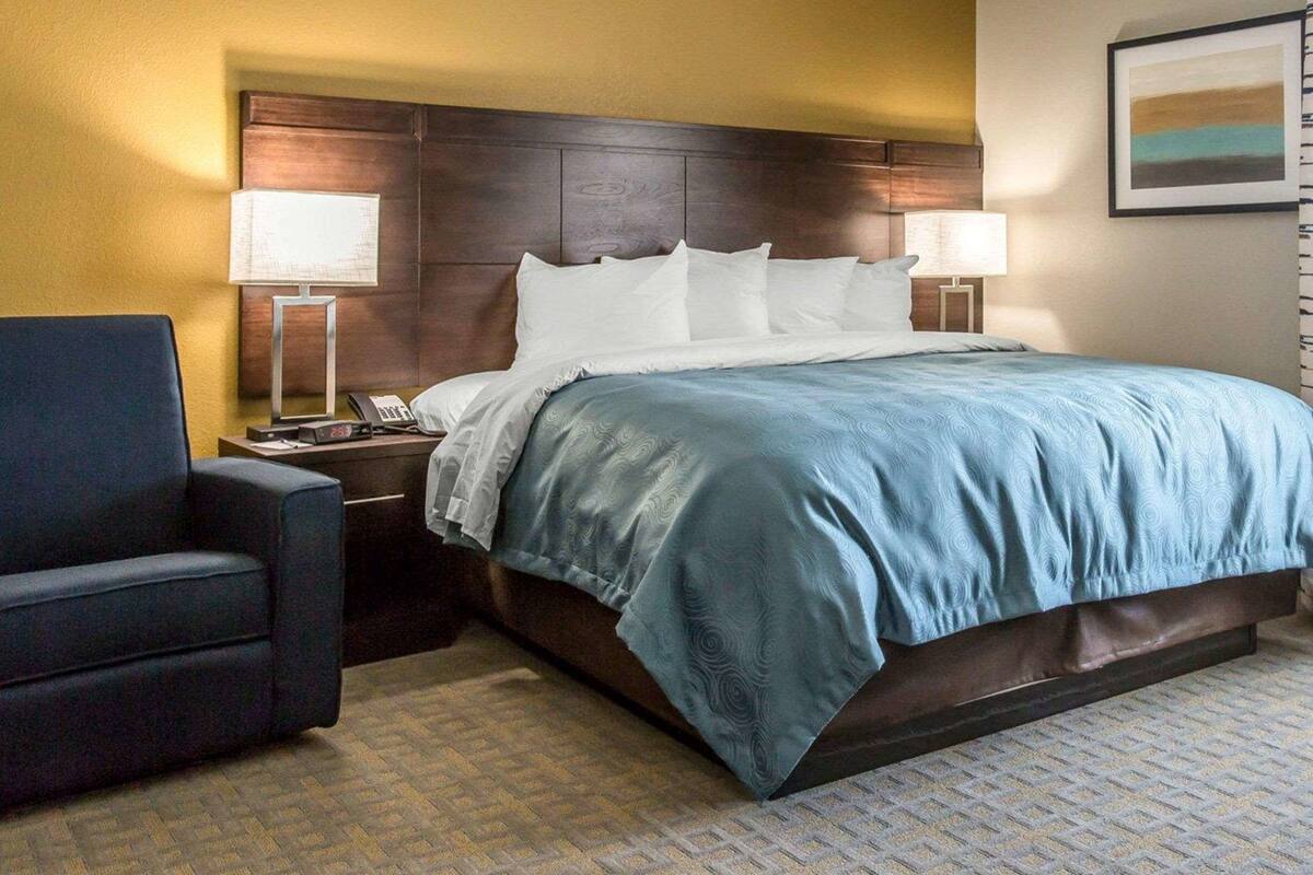 A hotel room with a large bed, two bedside tables, a chair, and a wall-mounted painting.