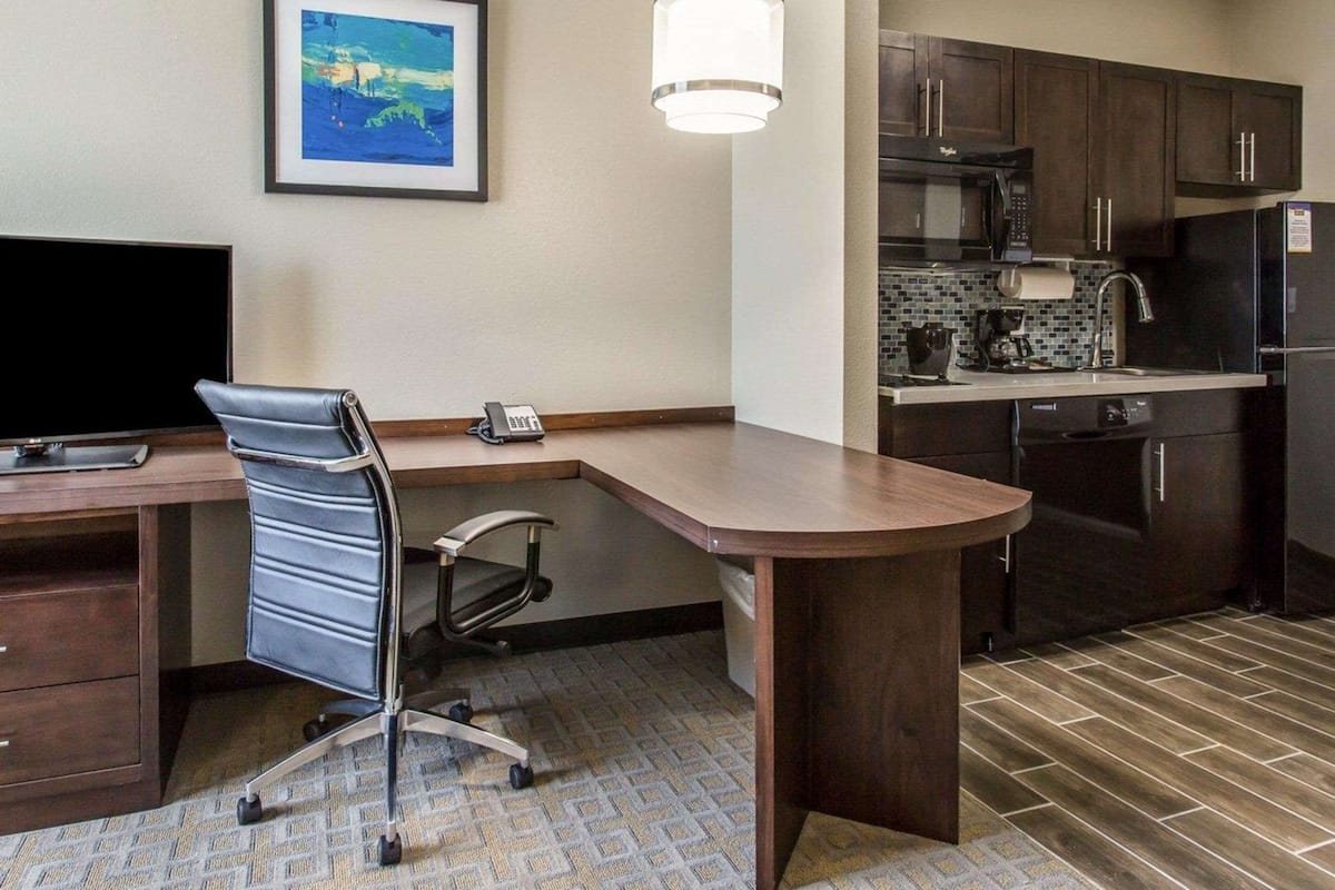 A hotel room with a desk, office chair, and a kitchenette.
