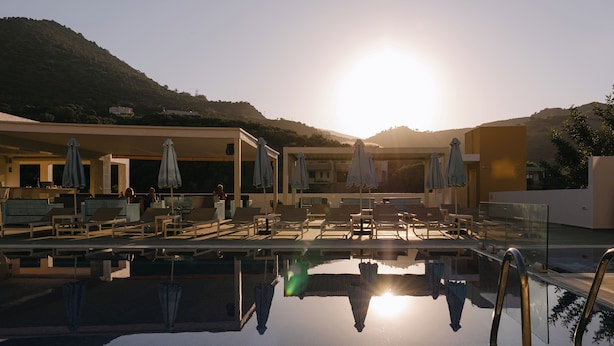 A pool area with lounge chairs and umbrellas, surrounded by buildings and hills. - Xidas Garden  (Mylopotamos)