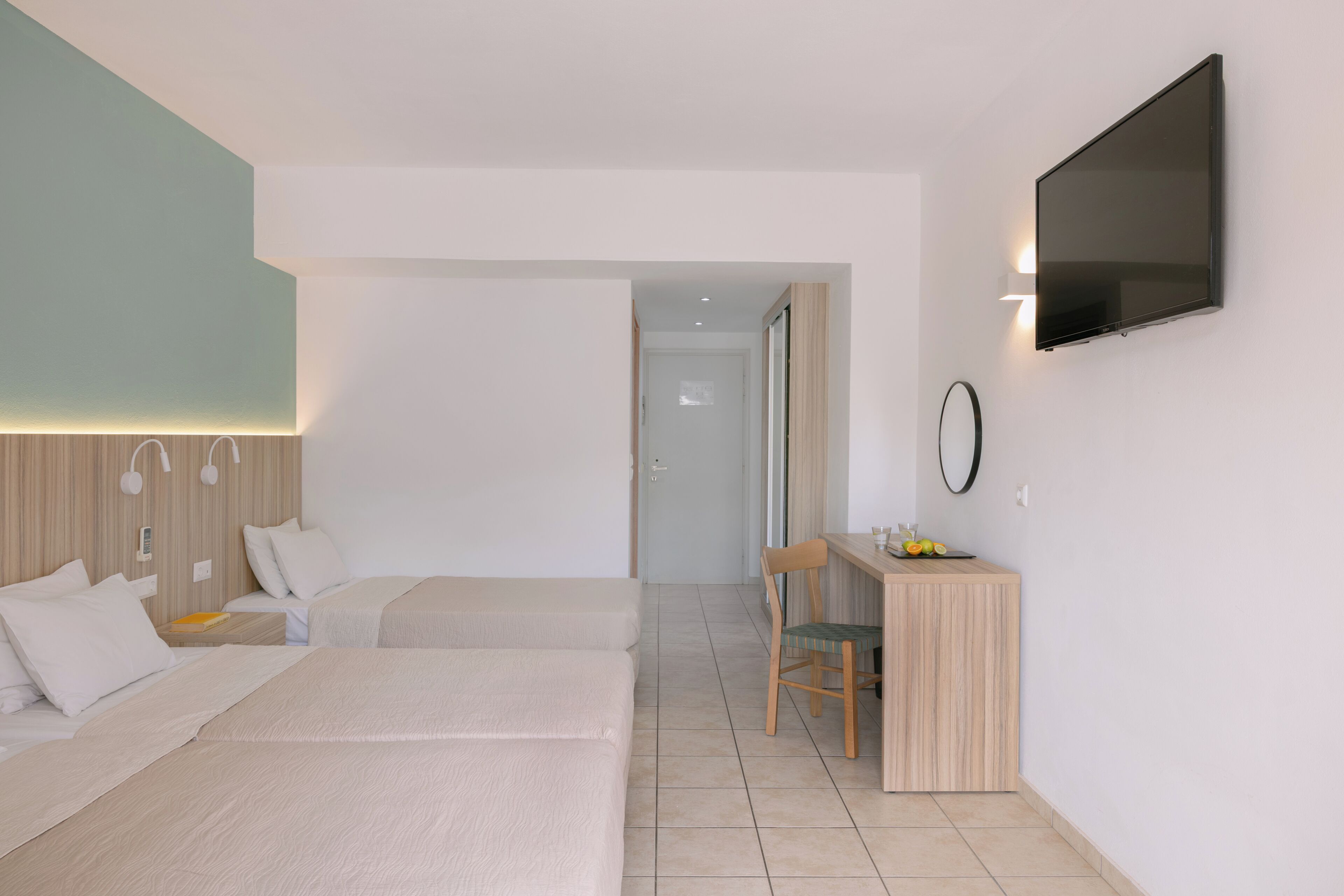 A hotel room with two beds, a desk with a chair, a flat-screen TV, and a mirror on the wall.