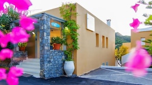 A modern building with a stone facade, a blue sign, and potted plants. - Xidas Garden  (Mylopotamos)