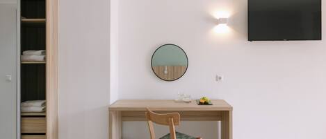 A room with a wooden desk, a chair, a round mirror, and a flat-screen TV mounted on the wall.
