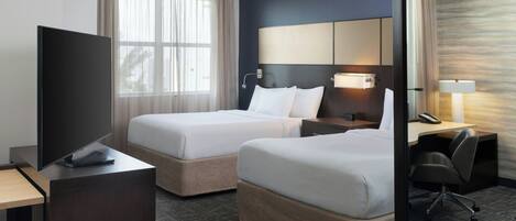 A hotel room with two beds, a desk, a TV, and a mirror.