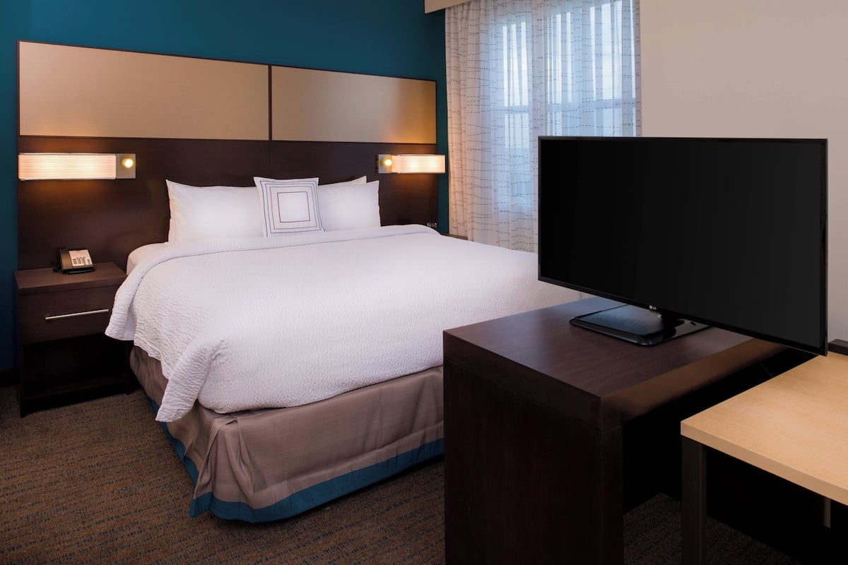 A hotel room with a bed, bedside lamps, a TV, and a desk.