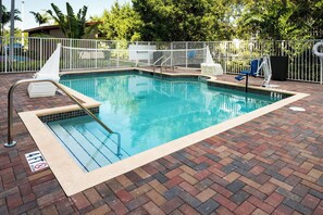 A rectangular swimming pool with a tiled edge, surrounded by a white fence, and a brick patio.