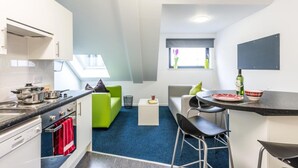Eine kompakte Küche mit modernen Geräten, ein Essbereich mit Barhocker und ein grünes Sofa.