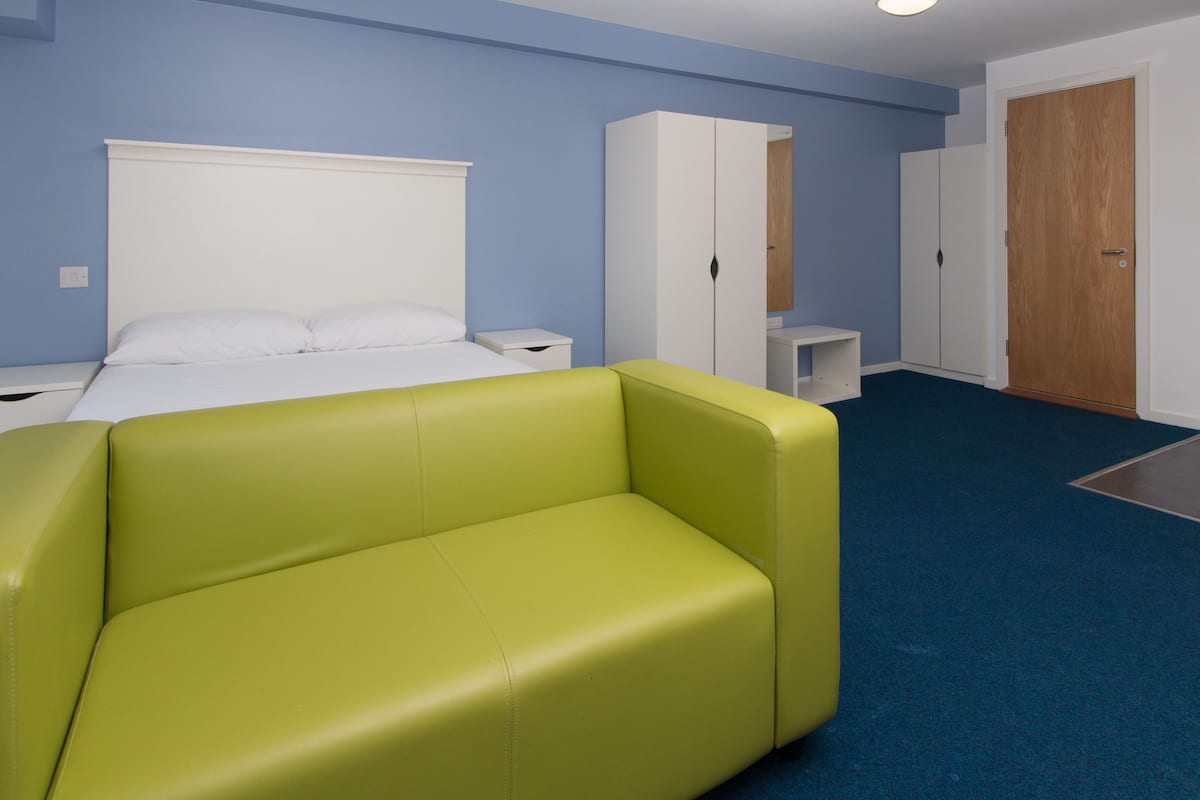 A hotel room with a bed, a green sofa, a wardrobe, and a door.
