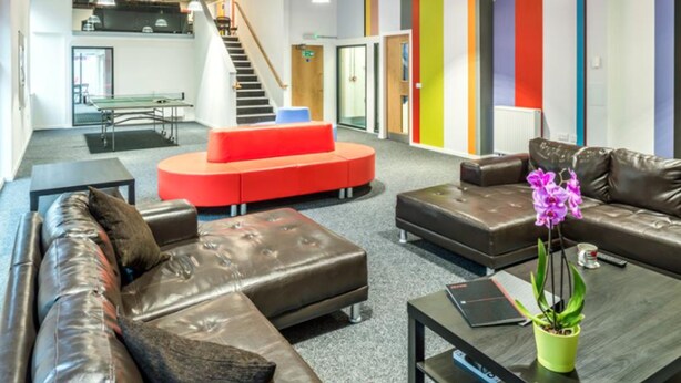 Ein moderner Arbeitsraum mit Ledersofas, einer roten, runden Sitzgruppe und einer Treppe.