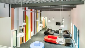 Ein moderner, offener Arbeitsbereich mit farbenfrohen Wänden, einer zentralen Sitzecke mit Sofas und Pendelleuchten.