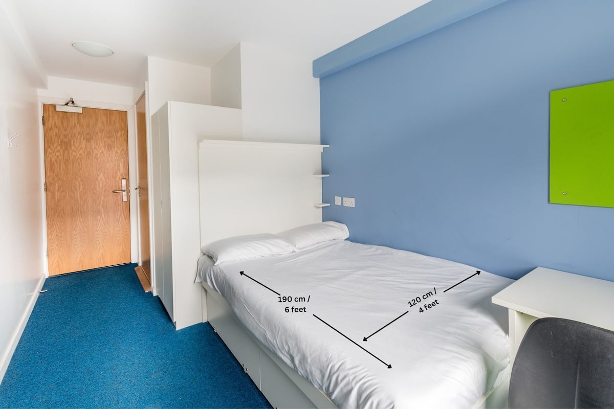 A compact hotel room with a single bed measuring 190 cm / 6 feet in length and 120 cm / 4 feet in width.