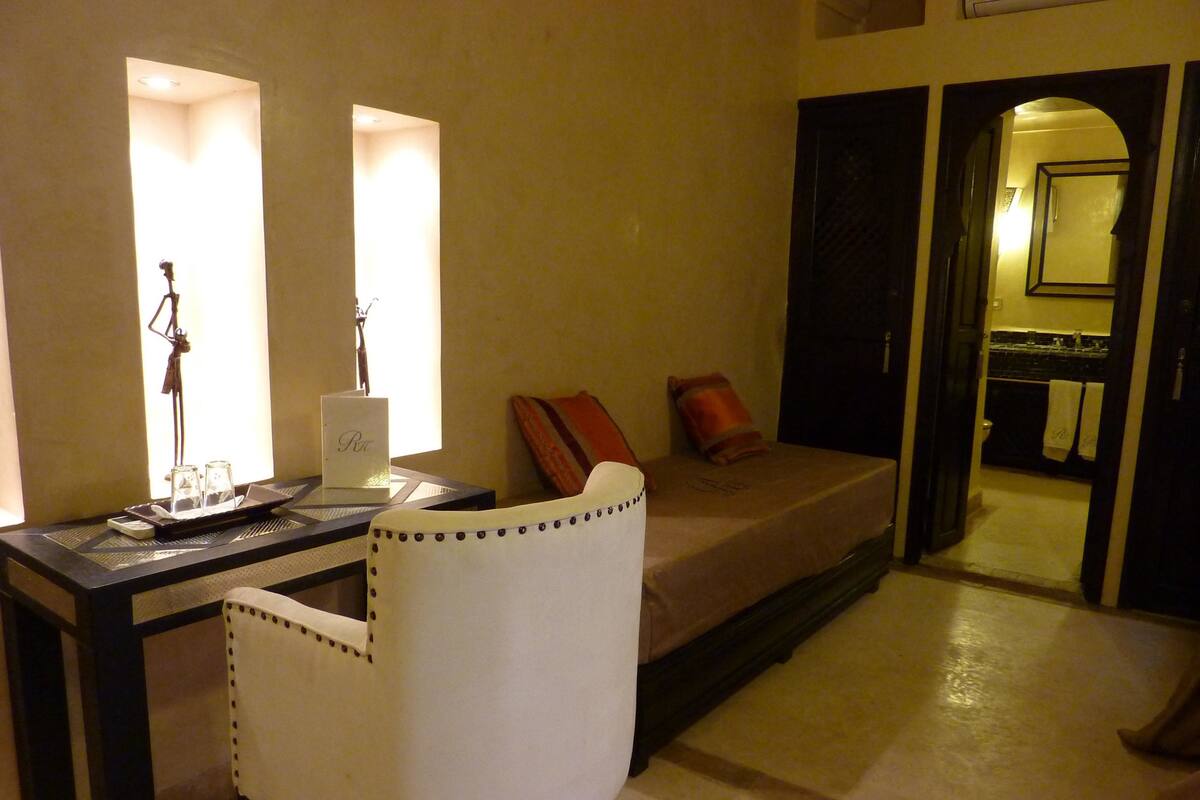 Une chambre d’hôtel comprenant un lit, un bureau avec une chaise, une petite table avec un plateau de verres et un miroir.