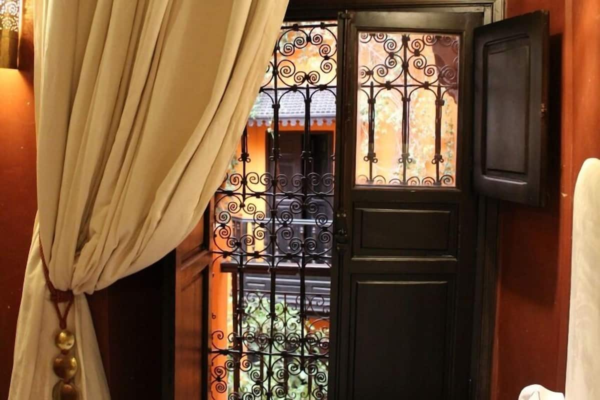 Une pièce dotée d’une fenêtre ornée de grilles en fer forgé, d’un rideau et d’un luminaire fixé au mur.