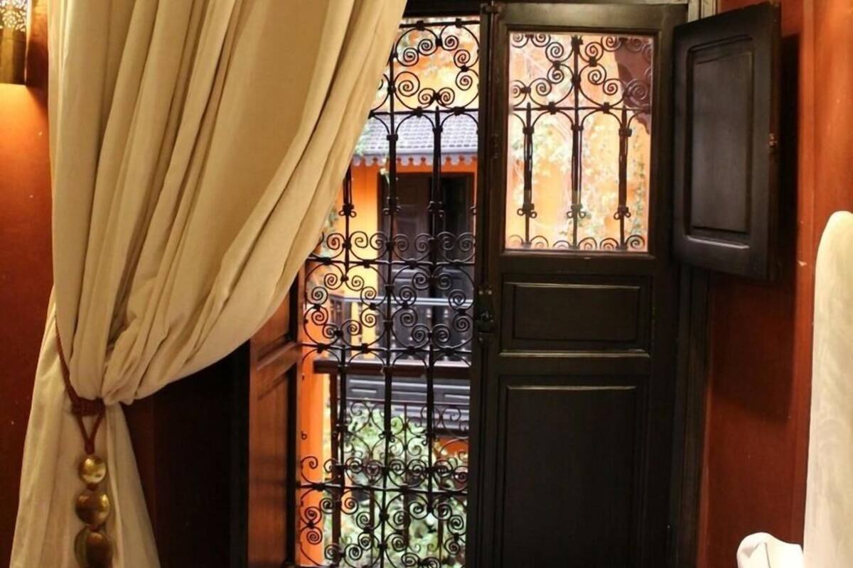 Une pièce avec un lit, une fenêtre ornée de barreaux en fer décoratifs, une lanterne suspendue et un rideau.