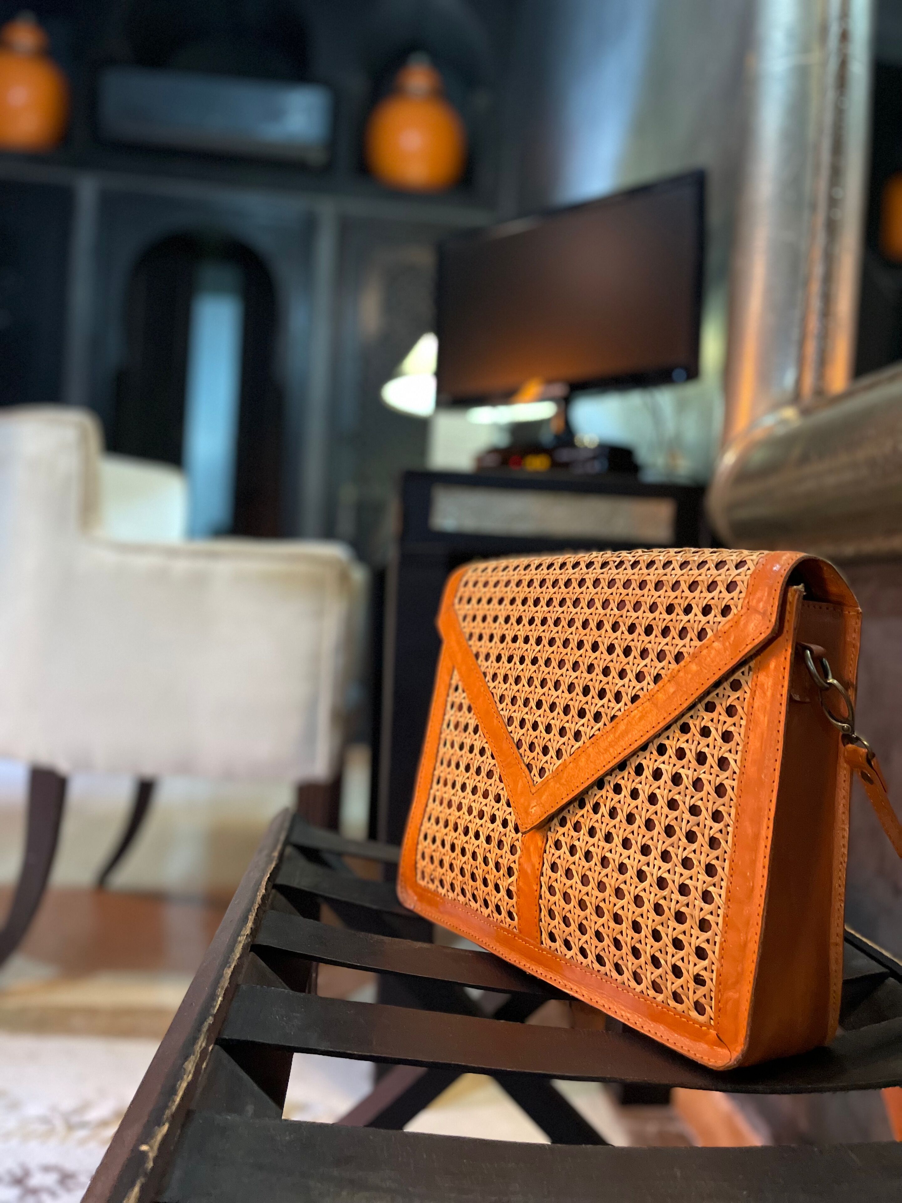 Un bolso de mimbre sobre una mesa de metal en una habitación con una televisión y una silla.