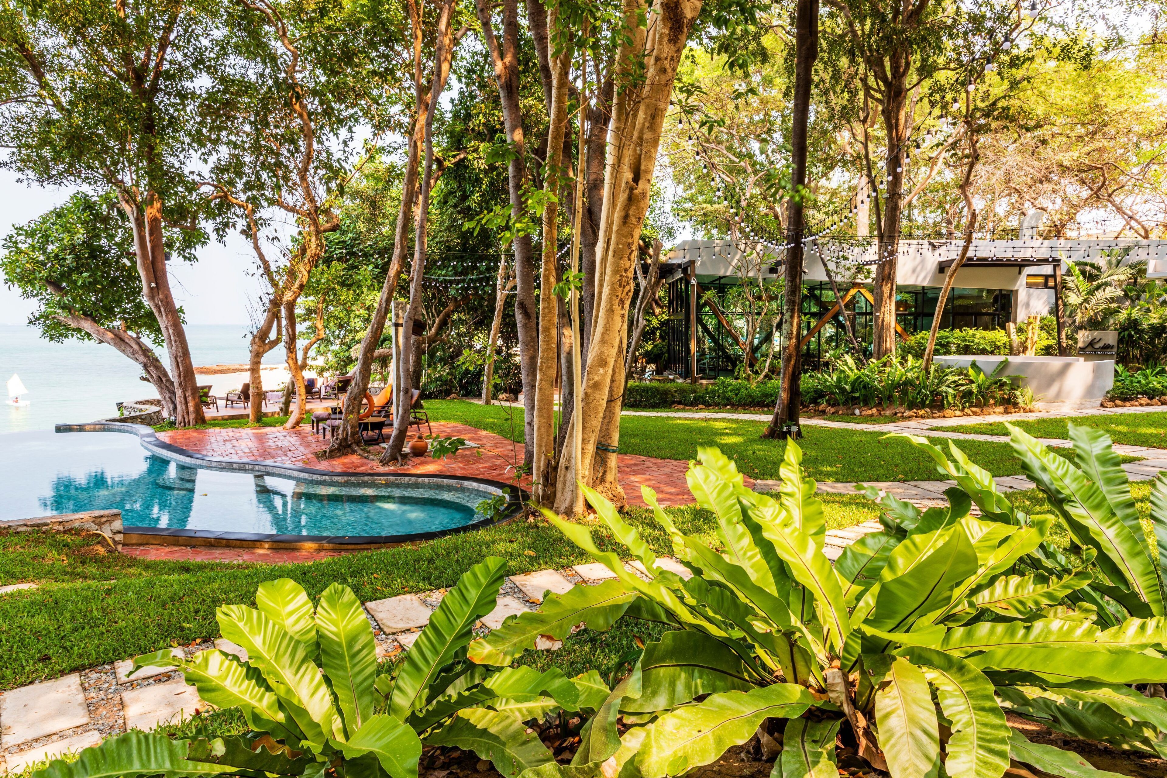 A pool surrounded by lush greenery and a modern building with a covered patio area.