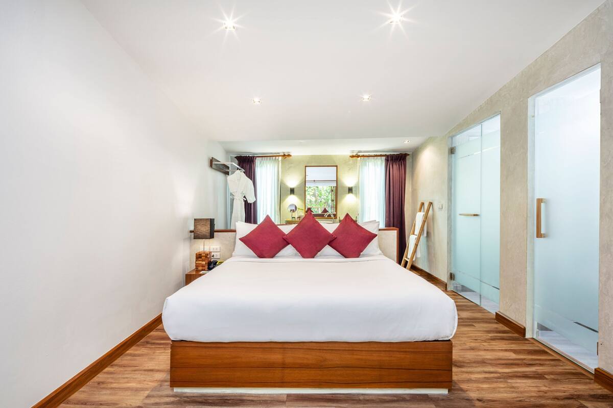 A modern hotel room with a large bed, wooden flooring, a large mirror, and a view of the outdoors.