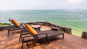 A deck with wicker lounge chairs and a small table, overlooking a body of water with a distant shoreline. - The Monttra Pattaya (Pattaya)