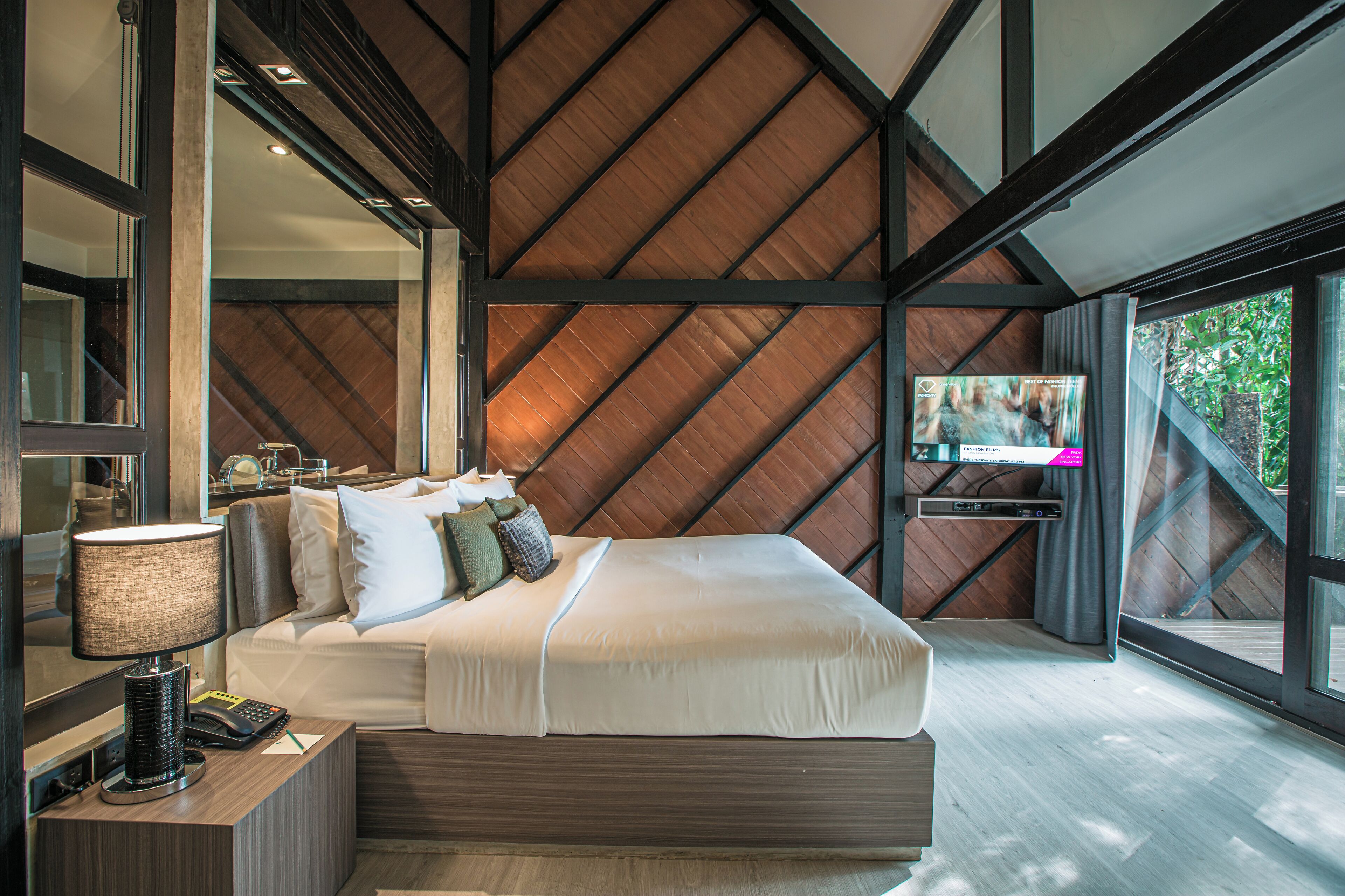A modern bedroom with a large bed, a television, and a view of the outdoors.