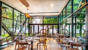 A restaurant with large windows, wooden tables, and chairs, overlooking a scenic view. - The Monttra Pattaya (Pattaya)