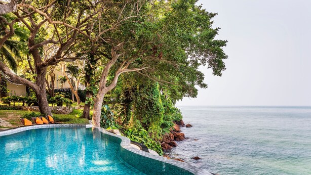 A poolside area with a curved edge, surrounded by lush greenery and a view of the sea. - The Monttra Pattaya (Pattaya)