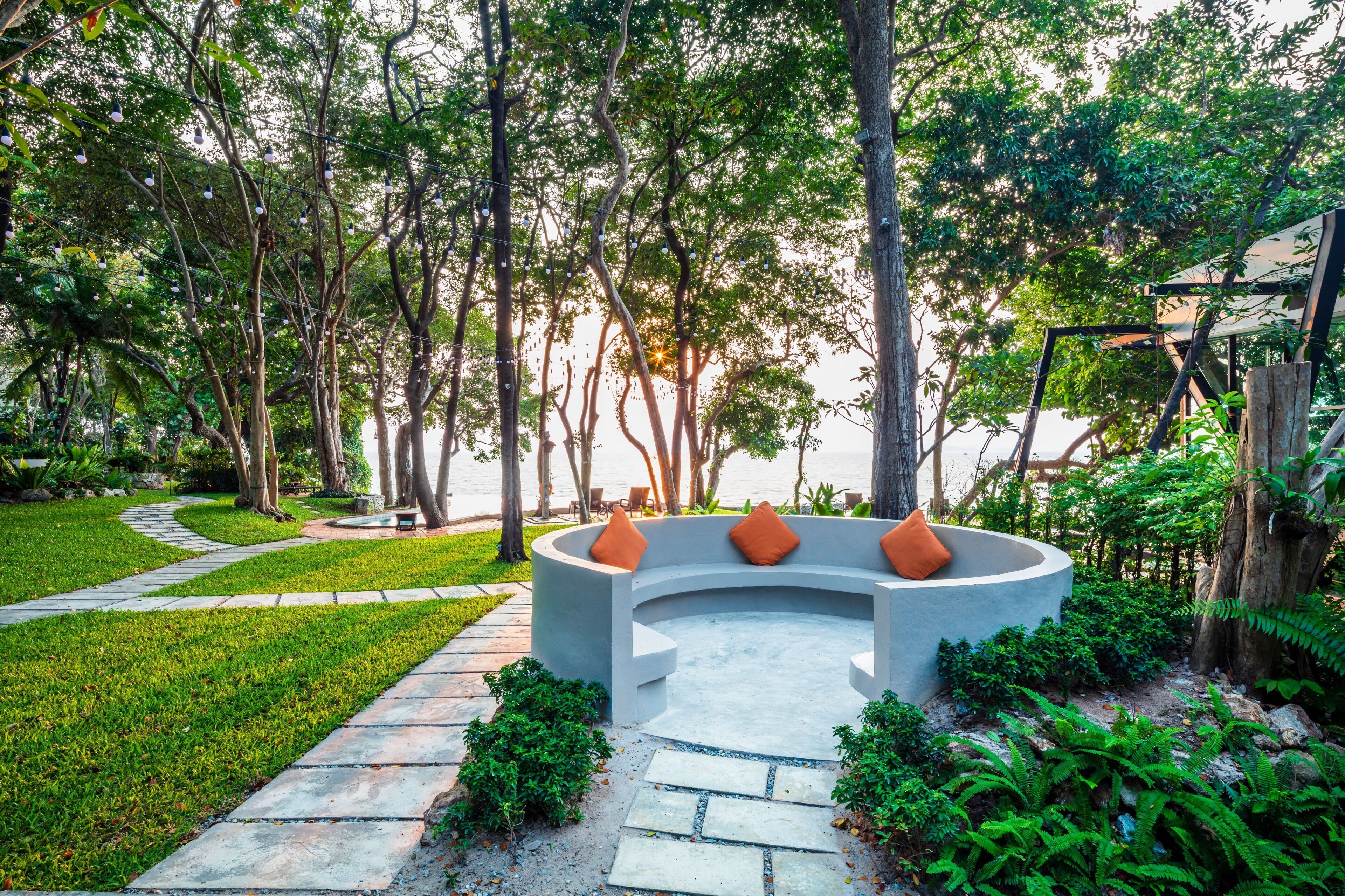 A circular seating area with orange cushions, surrounded by a stone pathway and lush greenery.