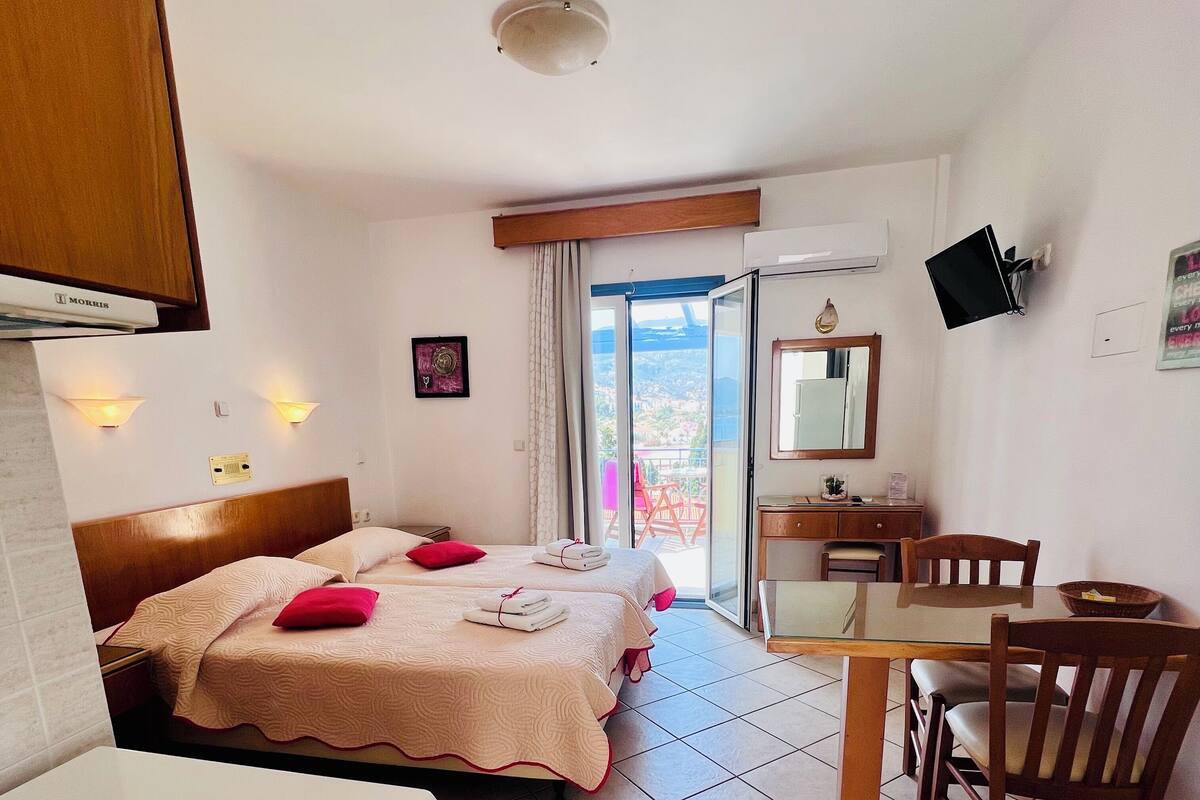 Quarto de hotel com cama, escrivaninha, cadeira, televisão e vista para o exterior.