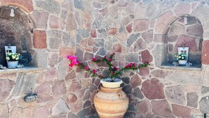 A stone wall with a large terracotta pot containing pink flowers. - KTM Sunny Villas (Poros)