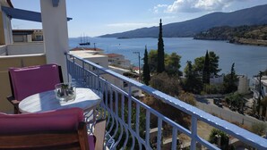 A balcony with a table and chairs, overlooking a body of water and hills. - KTM Sunny Villas (Poros)