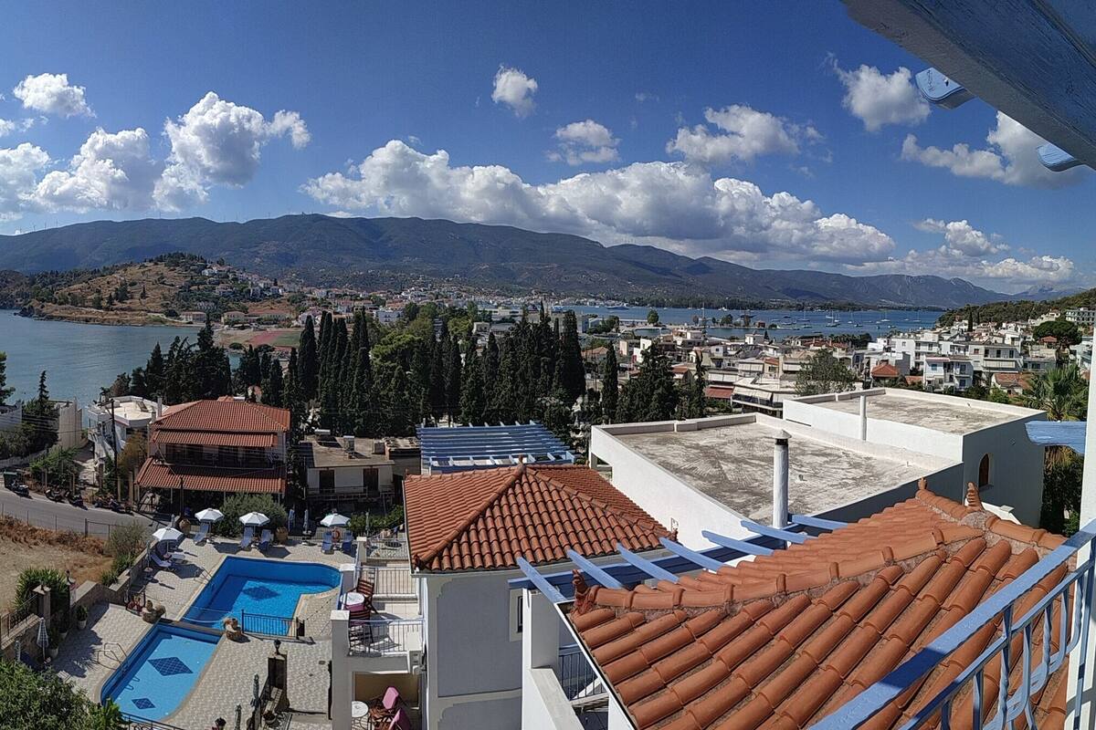 Vista de uma cidade costeira com piscina, edifícios em terraços e uma montanha ao fundo.