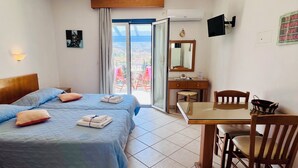 A hotel room with two beds, a desk with a chair, a TV, and a balcony with a view. - KTM Sunny Villas (Poros)