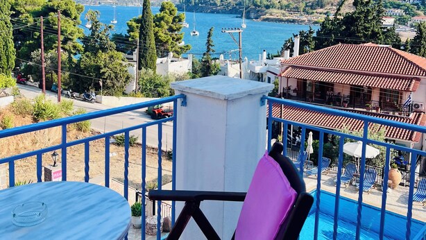 A balcony with a view of a body of water, a pool, and surrounding landscape. - KTM Sunny Villas (Poros)