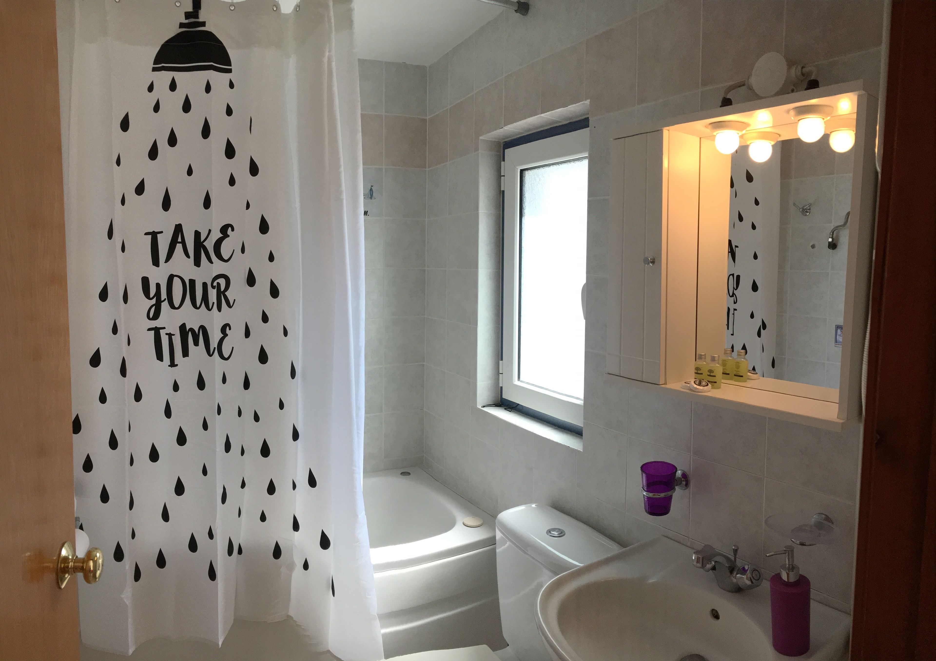 Un baño con cortina de ducha, una ventana, bañera, lavabo y espejo con iluminación.