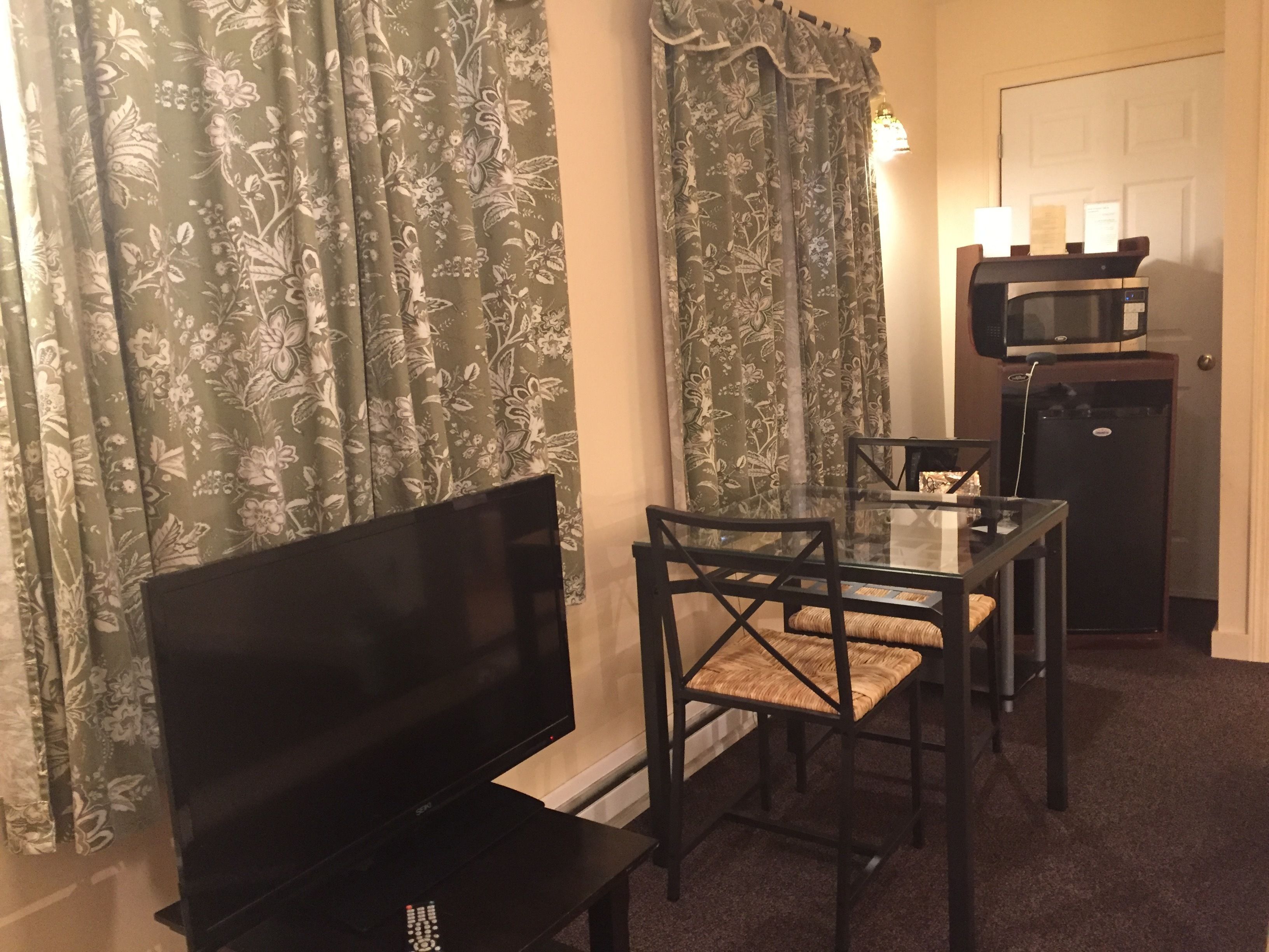 A small room with a TV, a table with chairs, a microwave, and floral curtains.