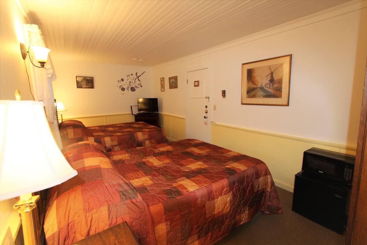 Ein Hotelzimmer mit zwei Betten, einem Fernseher, einem Gemälde und einer Lampe.