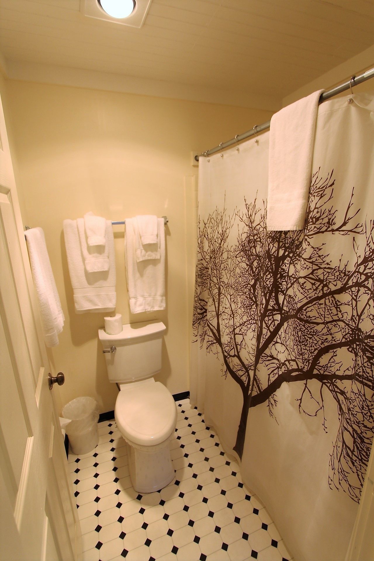 Un baño con inodoro, cortina de ducha con diseño de árbol y suelo de baldosas.